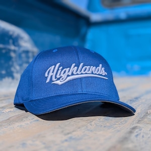 Op de afbeelding: Koningsblauwe baseballcap met het woord "Highlands" in witte letters geborduurd. De cap heeft een gebogen klep en een gestructureerde pasvorm. Een stijlvol accessoire.