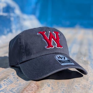 May include: A dark gray baseball cap with a red and white embroidered "W" logo on the front. The cap has a curved brim and an adjustable strap. The brand tag "47 CLEAN UP" is visible on the brim.