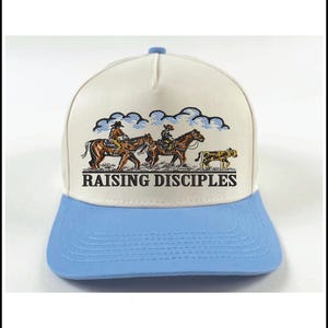 Puede incluir: Gorra de camionero blanca y azul claro con un gr&aacute;fico de vaqueros a caballo y un guepardo, bajo un cielo nublado. El texto "RAISING DISCIPLES" est&aacute; impreso en la parte delantera.