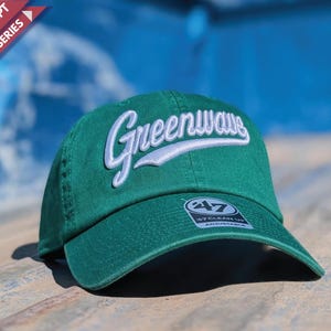 May include: A green baseball cap with the word "Greenwave" embroidered in white script across the front. The cap has a curved brim and an adjustable strap. The text "Retro Script Design Series" is in the upper left corner.