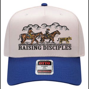 Puede incluir: Gorra de b&eacute;isbol con corona blanca y visera azul. La gorra presenta una ilustraci&oacute;n de vaqueros a caballo y el texto "RAISING DISCIPLES". La gorra tiene un ajuste cl&aacute;sico y est&aacute; hecha de tela de primera calidad.
