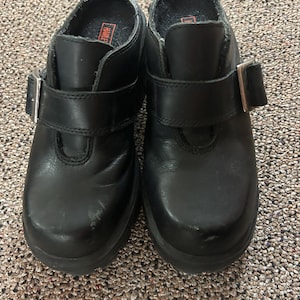 Könnte beinhalten: Paar schwarze Lederschuhe mit Schnallenverschluss. Die Schuhe haben eine runde Spitze und eine dicke Sohle. Im Inneren des Schuhs ist das Wort "Harley" auf der Innensohle aufgedruckt. Die Schuhe sind auf Komfort und Haltbarkeit ausgelegt.