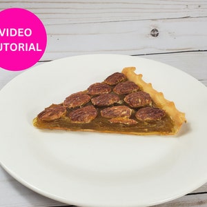 May include: A slice of pecan pie on a white plate. The pie has a golden crust and is filled with a brown pecan filling.