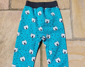 Op de afbeelding: Turquoise blauwe kinderbroek met een witte ijsbeerprint. De broek heeft een donkergrijze tailleband en boorden.