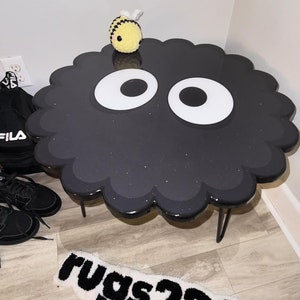 May include: Black and white cloud-shaped table with a black glitter finish and two large white eyes. A small yellow and black bee plush toy sits on top of the table.