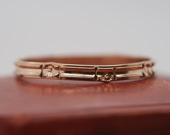 May include: A gold band ring with a decorative design. The ring is on a red velvet box.