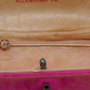 Puede incluir: Un broche de oro con una sola piedra transparente engastada en un dise&ntilde;o con forma de flor. El broche est&aacute; en una caja forrada de terciopelo.