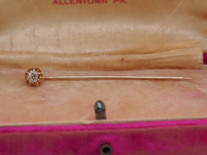 Puede incluir: Un broche de oro con una sola piedra transparente engastada en un dise&ntilde;o con forma de flor. El broche est&aacute; en una caja forrada de terciopelo.