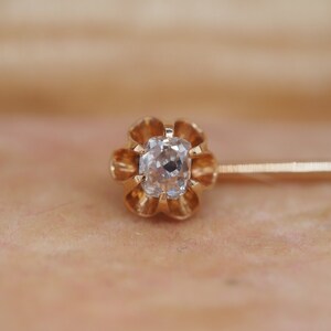 Puede incluir: Un broche de corbata de oro con una piedra preciosa transparente y facetada engastada en un dise&ntilde;o de flor.