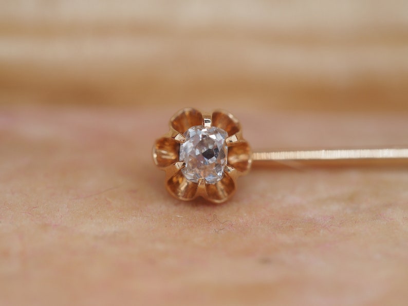 Puede incluir: Un broche de corbata de oro con una piedra preciosa transparente y facetada engastada en un dise&ntilde;o de flor.