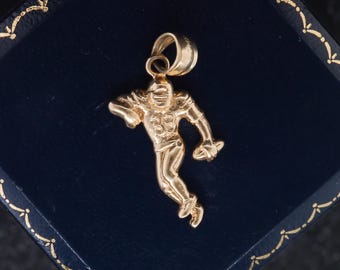Könnte beinhalten: Ein goldfarbener Metallanhänger in Form eines Footballspielers in Laufpose, der einen Helm und ein Trikot mit der gut sichtbaren Nummer 33 auf der Brust trägt. Die Figur hält einen Football in der Hand und hat eine große, runde Öse oben.