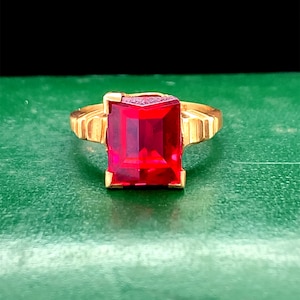 May include: A gold ring with a large, square, red gemstone.