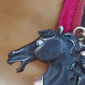 K&ouml;nnte beinhalten: Ein silberner Pferdekopf-Anh&auml;nger mit einem einzigen klaren Strassstein-Auge. Die M&auml;hne des Pferdes ist detailliert und der Anh&auml;nger ist an einer silbernen Kette befestigt.