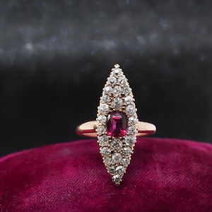 May include: A gold ring with a teardrop-shaped setting featuring a red ruby surrounded by a halo of small diamonds.