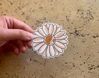 May include: A white daisy sticker with a brown center. The daisy has a simple, minimalist design.