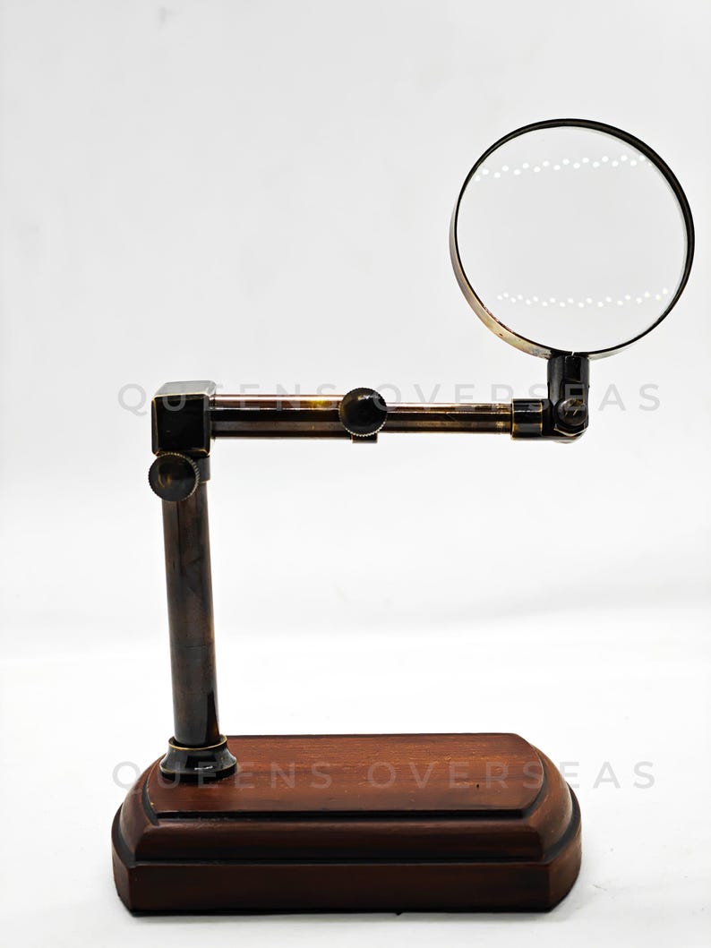 May include: A vintage-style magnifying glass with a dark wooden base and a brass-colored frame. The magnifying glass is round and mounted on an adjustable arm. The base is rectangular and has a dark brown finish.