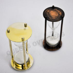 May include: Two hourglass sand timers, one with a brass finish and the other with a copper finish. Both have a clear glass bulb in the center.