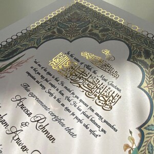 May include: A white wedding certificate with gold calligraphy and floral designs. The text reads "In the name of Allah, the Most Gracious...This agreement certifies that Aneesa Rehman & Ibrahim Anwar Khan marriage"