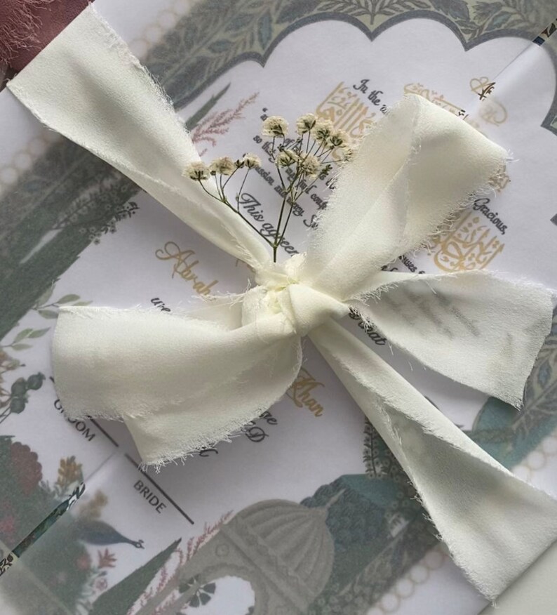 May include: A white ribbon tied in a bow with a small bouquet of white flowers on top. The ribbon is tied around a folded card with a floral design and the text "This occasion marks..." and "Abraham Khan".