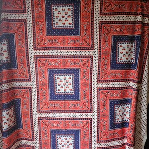 May include: A fabric with a repeating pattern of red, white, and navy blue squares. Each square features a central design of cherries and a decorative border. The background is white with small black dots.