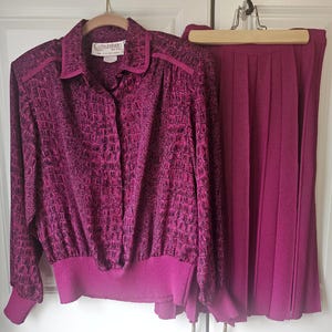 May include: A two-piece vintage magenta suit. The long-sleeved top features a textured, crocodile-like pattern and a button-down front. The matching pleated skirt hangs next to the top. The top has the brand name "Castleberry" on the label.