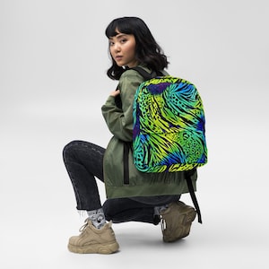 Può includere: Uno zaino con una vivace stampa animalier astratta nei toni del verde, blu e giallo. Lo zaino ha spallacci neri e un pannello posteriore nero. La borsa è indossata da una persona che indossa una giacca verde e jeans neri.