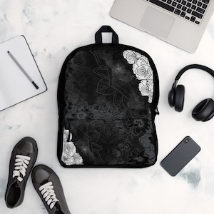 May include: Black backpack with a white floral pattern. The pattern features roses and leaves. The backpack has a zipper closure and adjustable straps.
