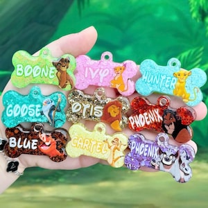 Puede incluir: Una colección de etiquetas para mascotas en forma de hueso con fondos brillantes e ilustraciones de personajes de dibujos animados. Cada etiqueta presenta un nombre diferente, incluyendo "Boone", "Ivy" y "Hunter". Las etiquetas son de varios colores, como verde, rosa y azul.