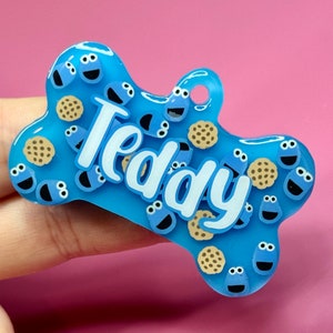 May include: Blue and white dog tag with the name "Teddy" and a cookie monster design.