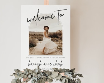 Può includere: Benvenuti al cartello di celebrazione di laurea con una foto di una persona in un abito bianco in piedi in un paesaggio desertico. Il cartello dice "Benvenuti a" in un font corsivo nero con un arco sopra la foto. Il testo sotto la foto dice "Per la celebrazione di laurea Hannah Anne Clark 6.10.2026".