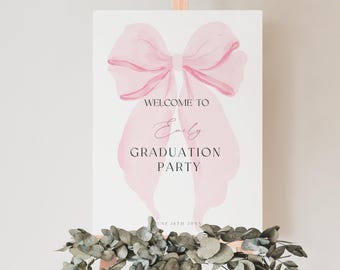 Può includere: Un cartello di benvenuto bianco con un fiocco rosa ad acquerello e il testo "Benvenuti alla festa di laurea di Emily".