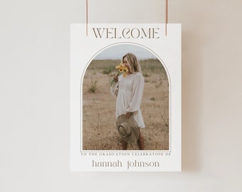 Könnte beinhalten: Willkommen zur Abschlussfeier von Hannah Johnson. Ein weißes Schild mit einem braunen Bogenrahmen, der ein Foto einer Frau in einem weißen Kleid zeigt, die gelbe Blumen auf einem Feld hält.
