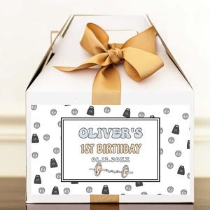May include: White gift box with a gold ribbon and a label that says "Oliver's 1st Birthday 01.13.20XX". The label has a pattern of small dumbbells and barbells.