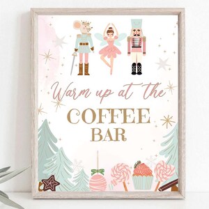 May include: A pink and white sign with a whimsical illustration of a mouse, a ballerina, and a nutcracker. The sign reads "Warm up at the Coffee Bar" and features a festive winter scene with candy canes, snowflakes, and trees.