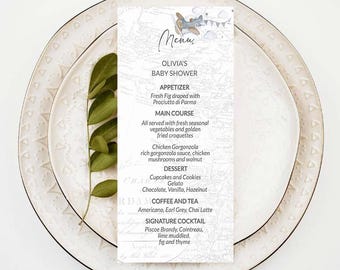 以下が含まれることがあります： 青い飛行機のイラストと「Menu」という文字が書かれた白いメニューカード。オリビアのベビーシャワーで提供される料理と飲み物が記載されています。メニューは、前菜、メインディッシュ、デザート、コーヒーと紅茶、そしてシグネチャーカクテルが含まれています。