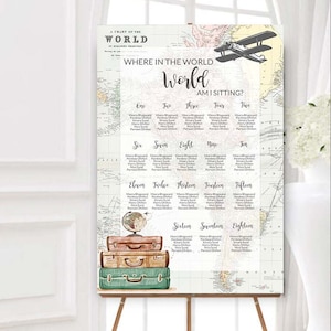 May include: A large wedding seating chart on an easel. The chart features a world map design with the text "Where in the World Am I Sitting?" and guest names. A stack of vintage suitcases and a globe are at the bottom.