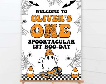 May include: A Halloween-themed sign on a wooden easel. The sign reads "Welcome to Oliver's One Spooktacular 1st Boo-Day" in orange and black. A ghost on a skateboard and candy corn are also featured.