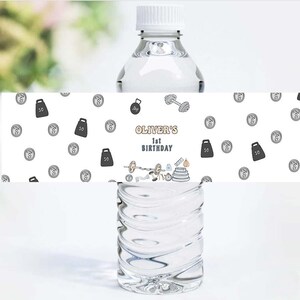 May include: Water bottle label with a white background and black and gray weightlifting themed illustrations. The label says "Oliver's 1st Birthday".