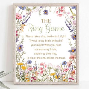 May include: A framed sign with the text "The Ring Game" surrounded by a floral border. The sign includes instructions for a game, with colorful flowers in shades of pink, purple, yellow, and blue.