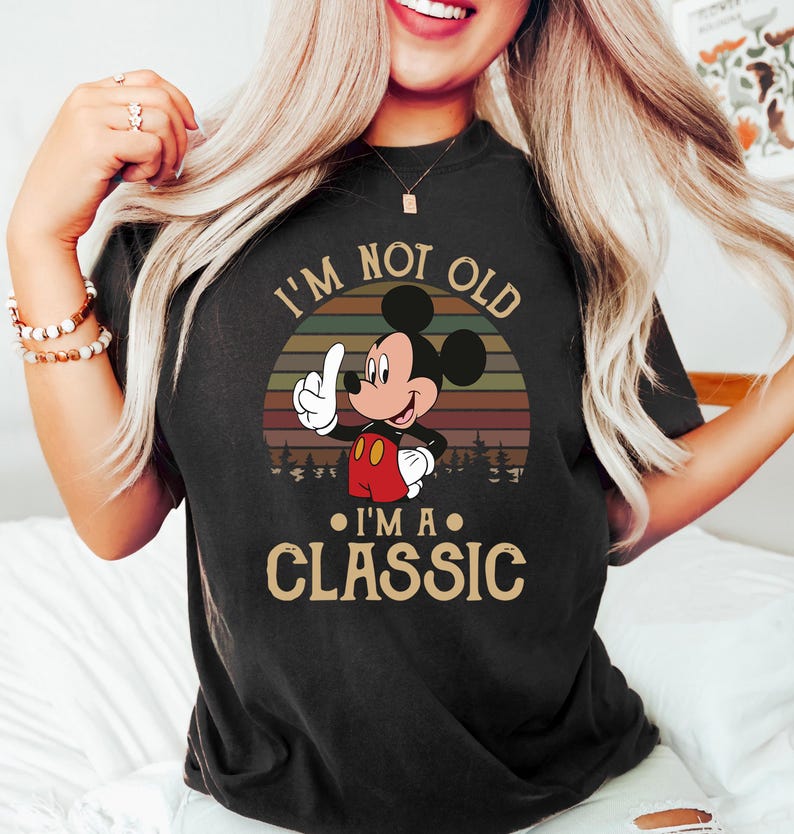 Puede incluir: Camiseta negra con Mickey Mouse y el texto "I'm Not Old, I'm a Classic." El dise&ntilde;o incluye un atardecer retro y una silueta de bosque. Mickey se&ntilde;ala hacia arriba, con pantalones cortos rojos y guantes blancos.
