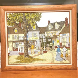 May include: A framed painting depicting a quaint town scene with a horse-drawn carriage in front of a building labeled "Coach Stop Inn". The painting features a tree, a general store, and two people walking in the street.