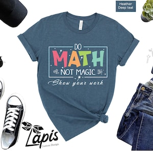 May include: A heather deep teal t-shirt with the text "Do Math Not Magic Show your work" in a colorful rainbow font. The text is inside a white rectangle with a white border.