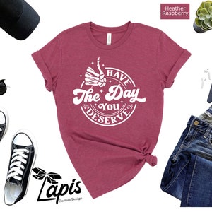 May include: A heather raspberry t-shirt with a white graphic that says "I Have The Day You Deserve" with a thumbs up hand and stars around it.