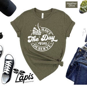 May include: A green t-shirt with a white graphic that says "Have the Day You Deserve" with a skeleton hand giving a thumbs up.