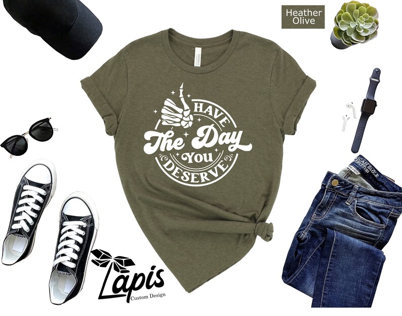 May include: A green t-shirt with a white graphic that says "Have the Day You Deserve" with a skeleton hand giving a thumbs up.