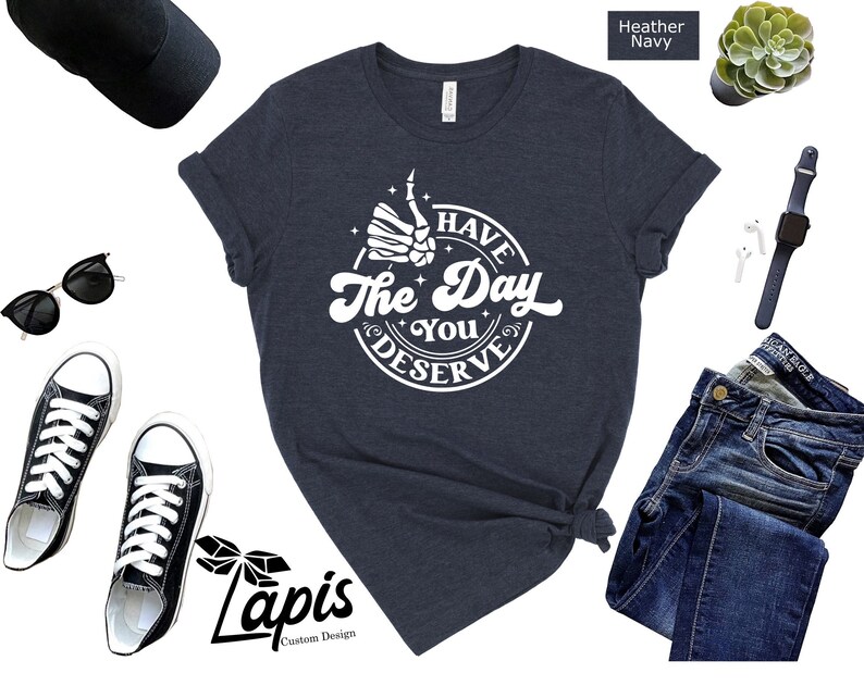 May include: A heather navy blue t-shirt with a white graphic that says "Have the Day You Deserve" with a skeleton hand giving a thumbs up.