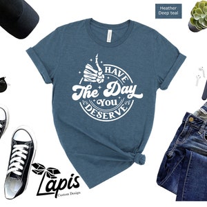 May include: A heather deep teal t-shirt with a white graphic that says "Have the Day You Deserve" with a skeleton hand giving a thumbs up.
