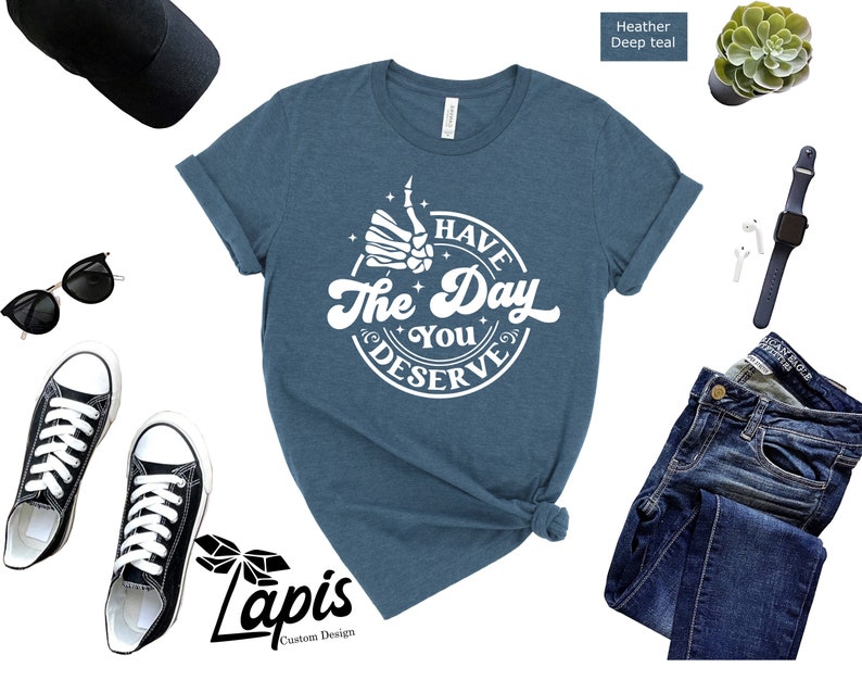 May include: A heather deep teal t-shirt with a white graphic that says "Have the Day You Deserve" with a skeleton hand giving a thumbs up.