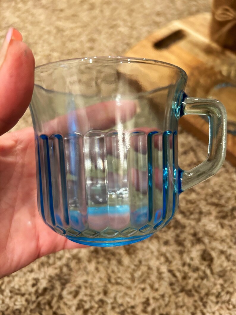 May include: A clear glass mug with a blue rim and vertical lines. The mug has a handle.