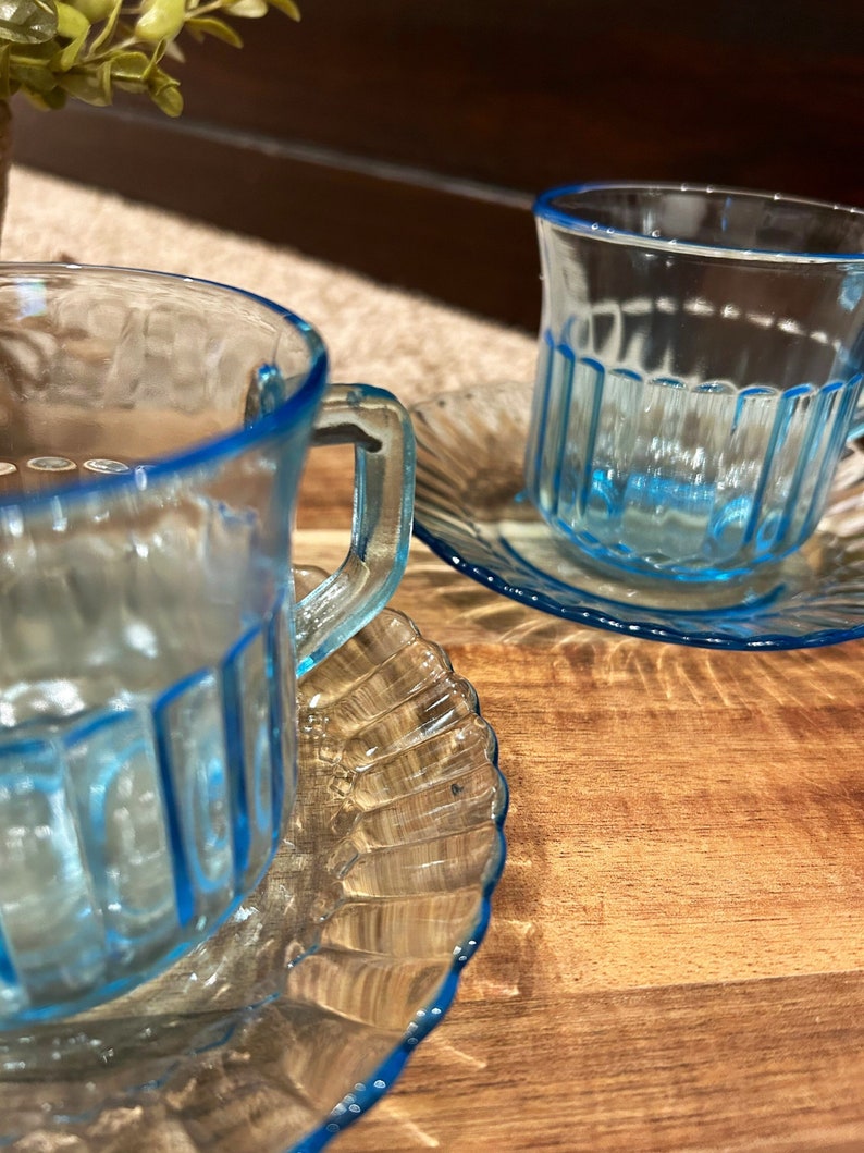 May include: Two blue glass teacups with matching saucers. The cups and saucers have a textured, ribbed design and a blue rim.